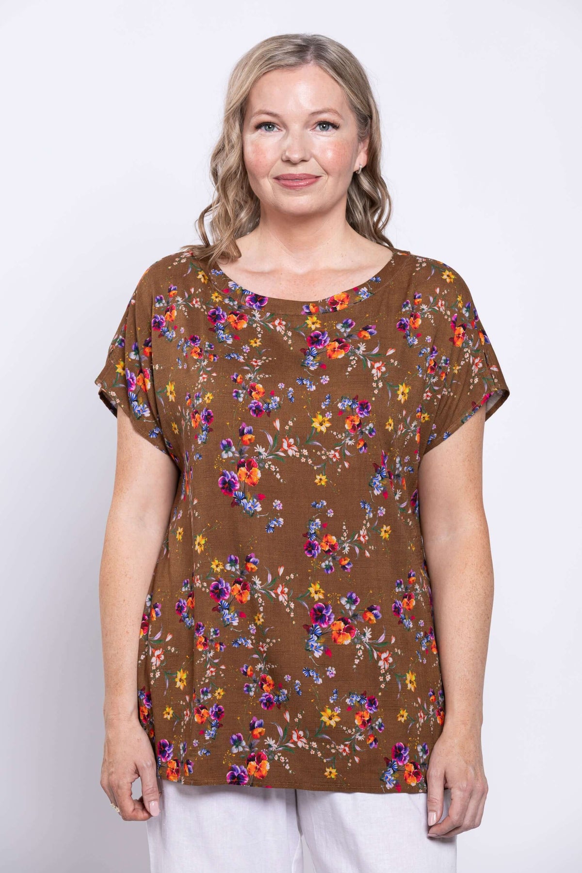 Close-up front view of model wearing a brown floral top and white pants against a white background