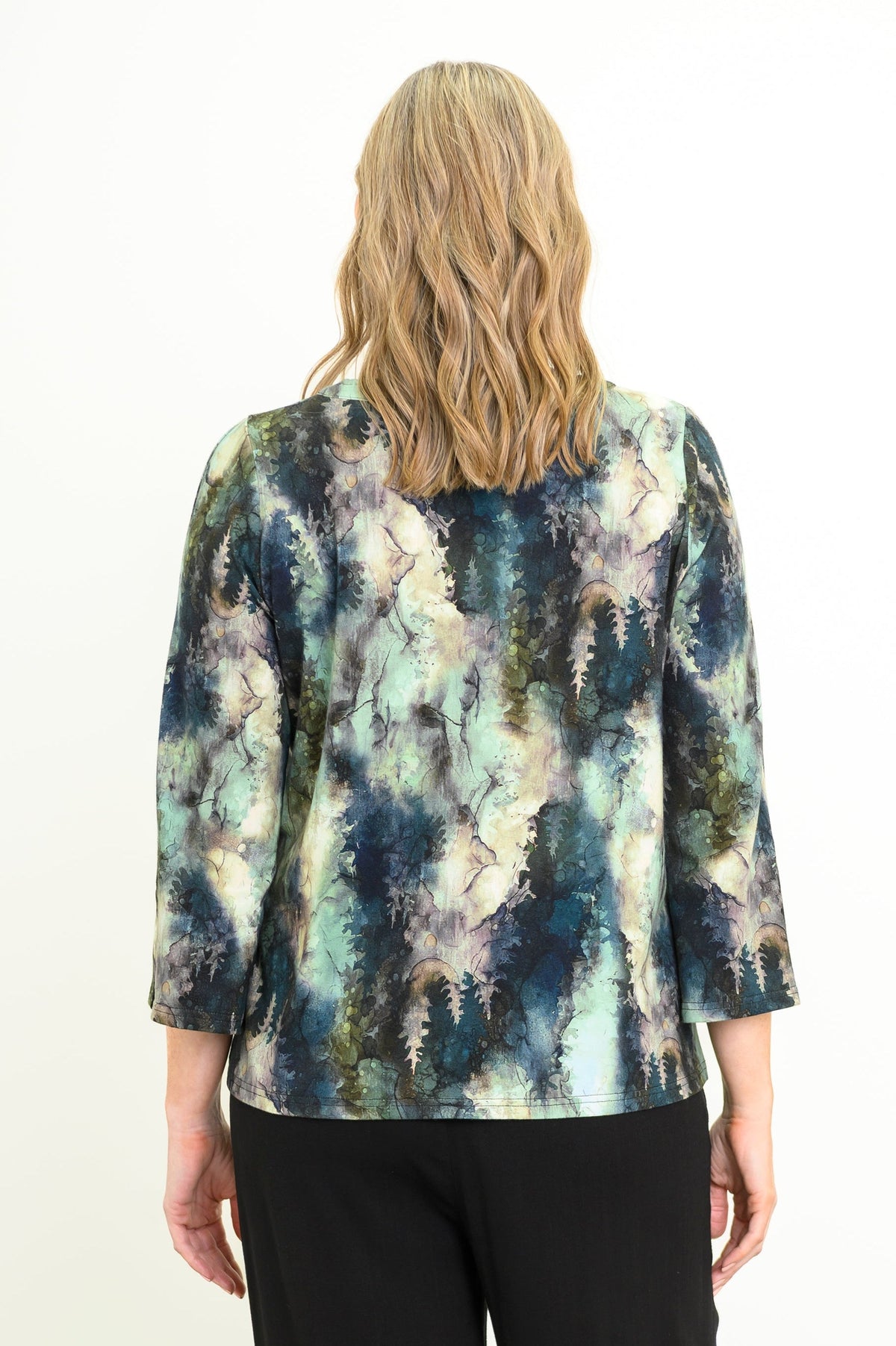 Back view of a female model wearing a watercolor green top with long sleeves with black pants, against a white backdrop