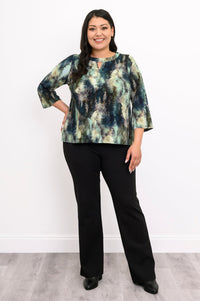 Front view of a female model wearing a watercolor green top with long sleeves with black pants and heels, against a white wall and gray floor