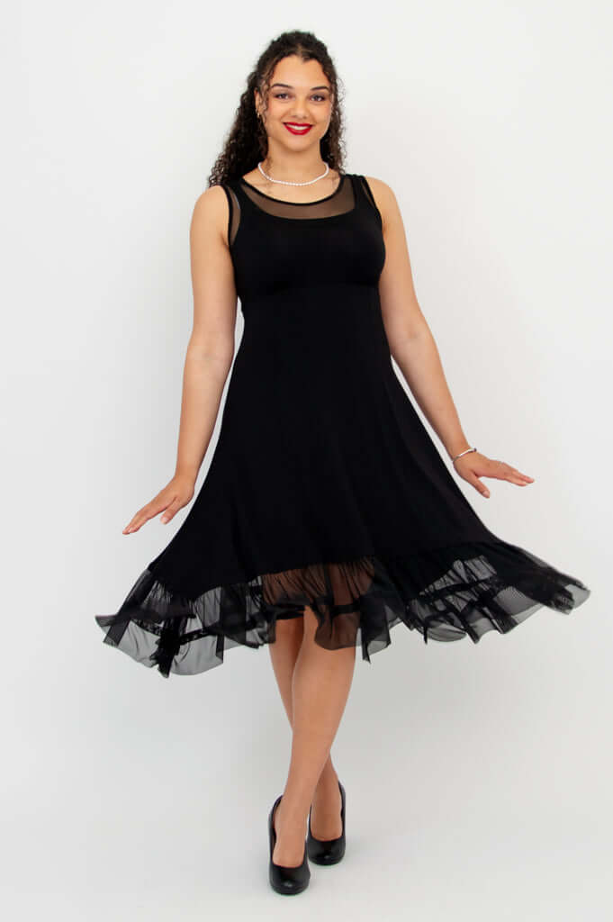 Model twirling in black sleeveless dress with mesh hem and layered look