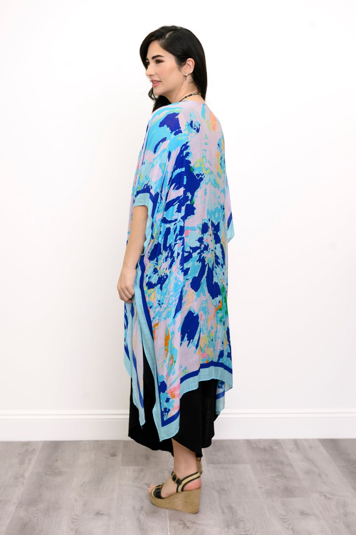 Back view of woman wearing a blue floral kimono on a black outfit against a white background