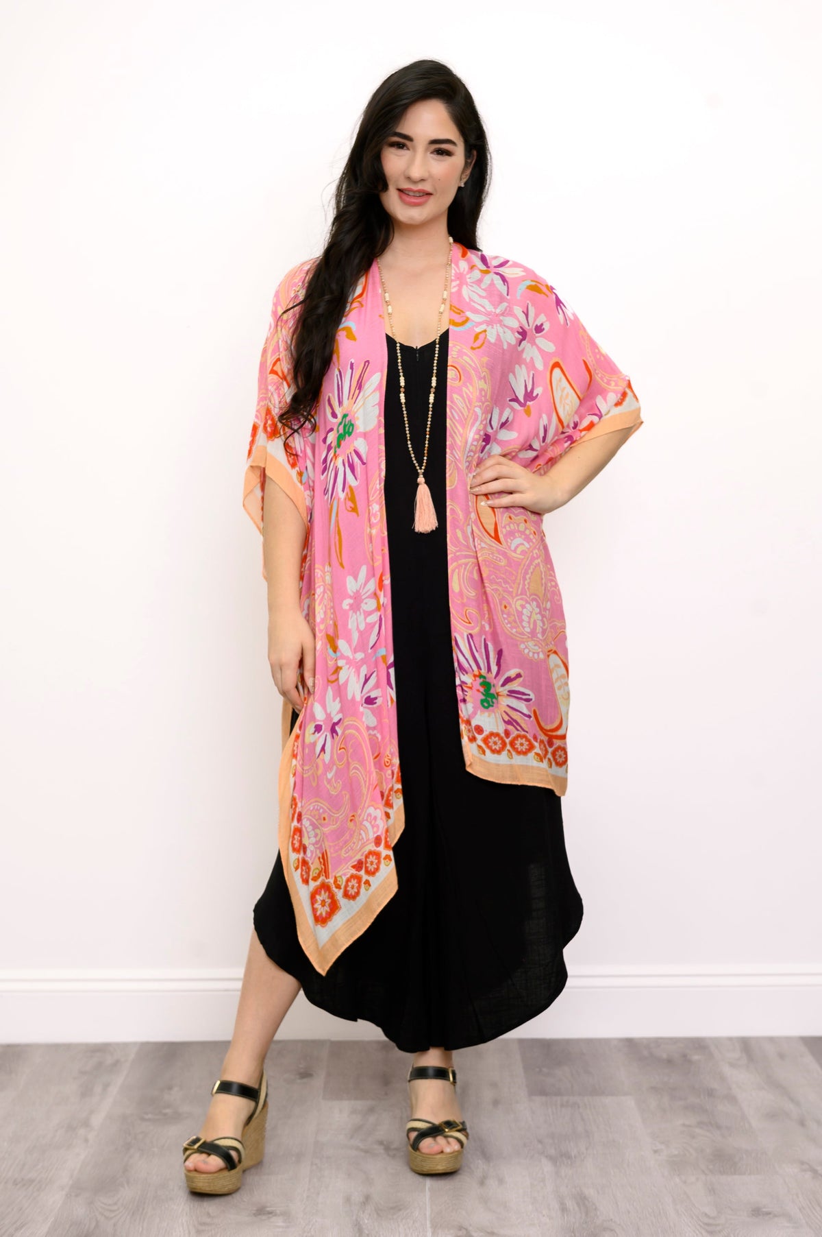 Front view of woman wearing a pink floral kimono on a black outfit against a white background