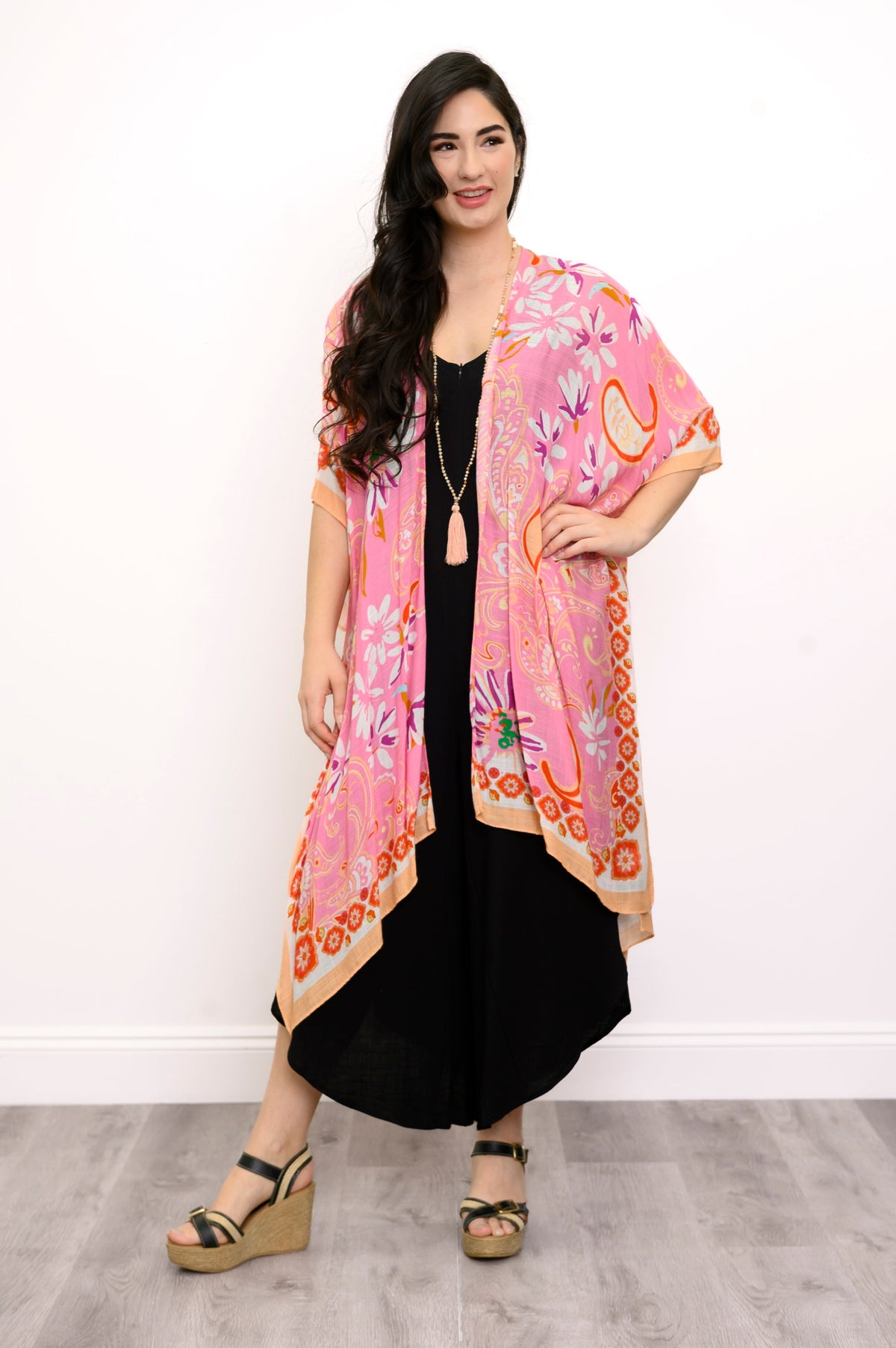 Front view of woman wearing a pink floral kimono on a black outfit against a white background