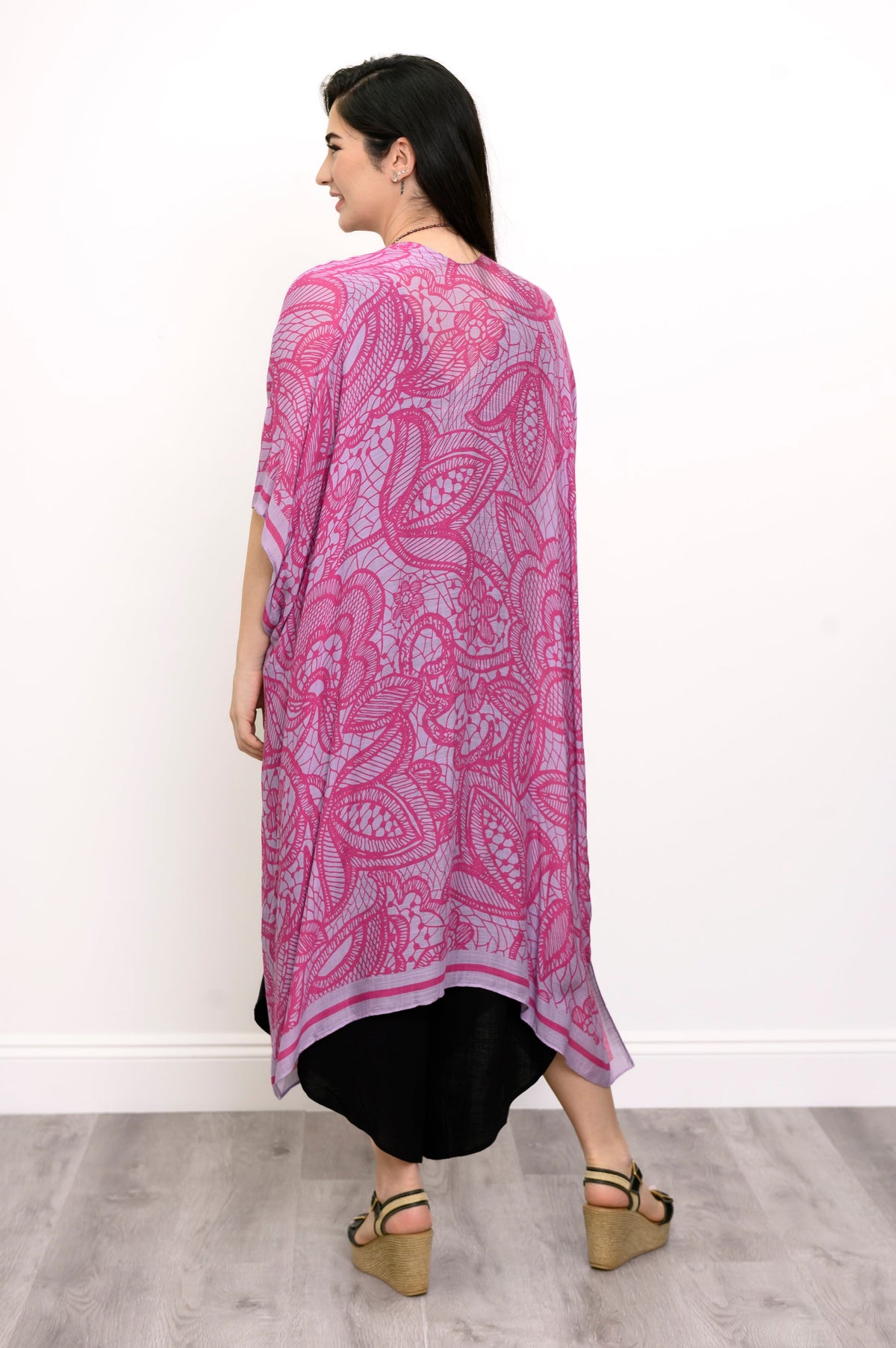 Back view of woman wearing pink and purple lace patterned kimono on a black outfit against a white background