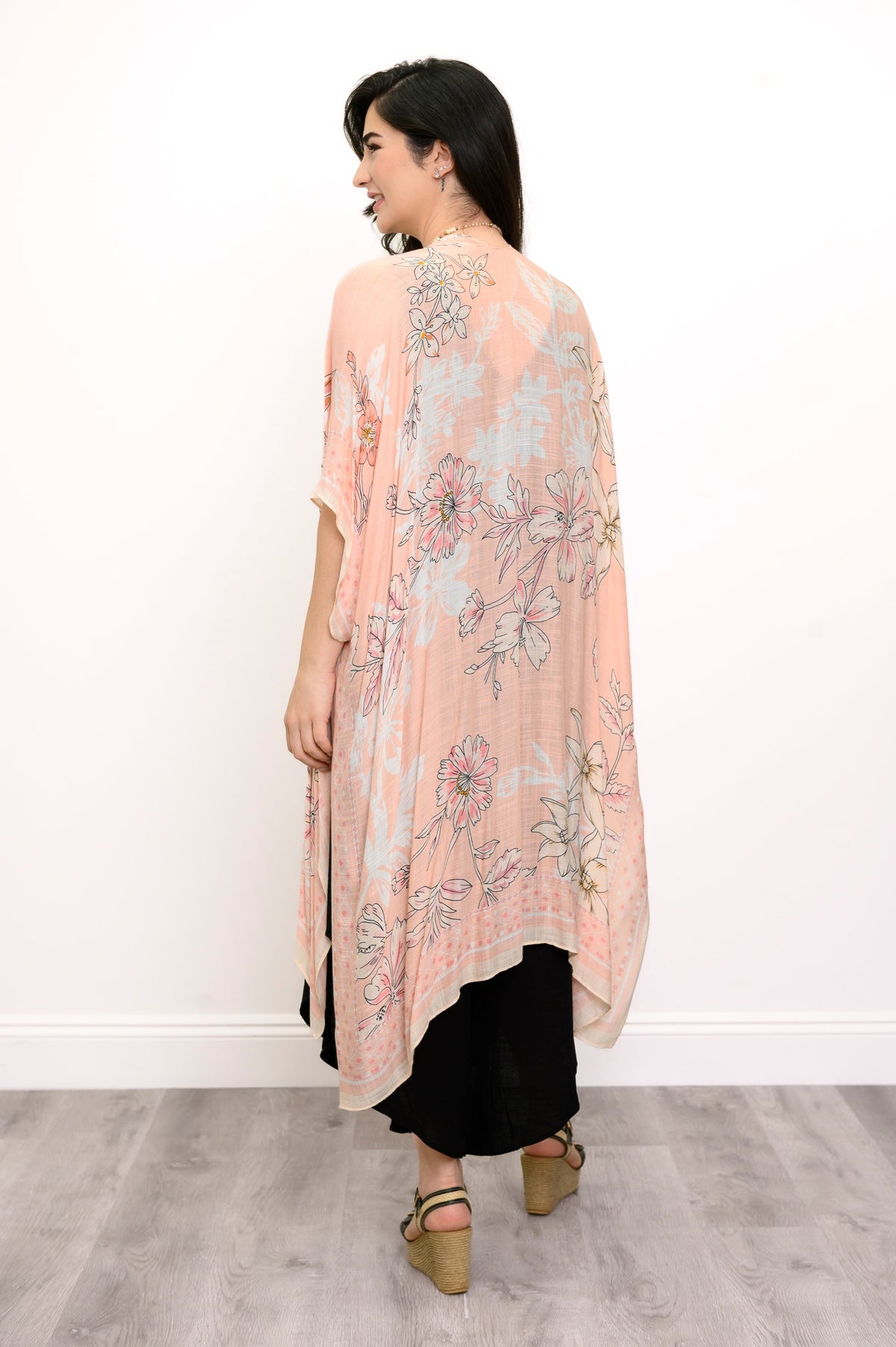 Back view of woman wearing pink floral patterned kimono on a black outfit against a white background