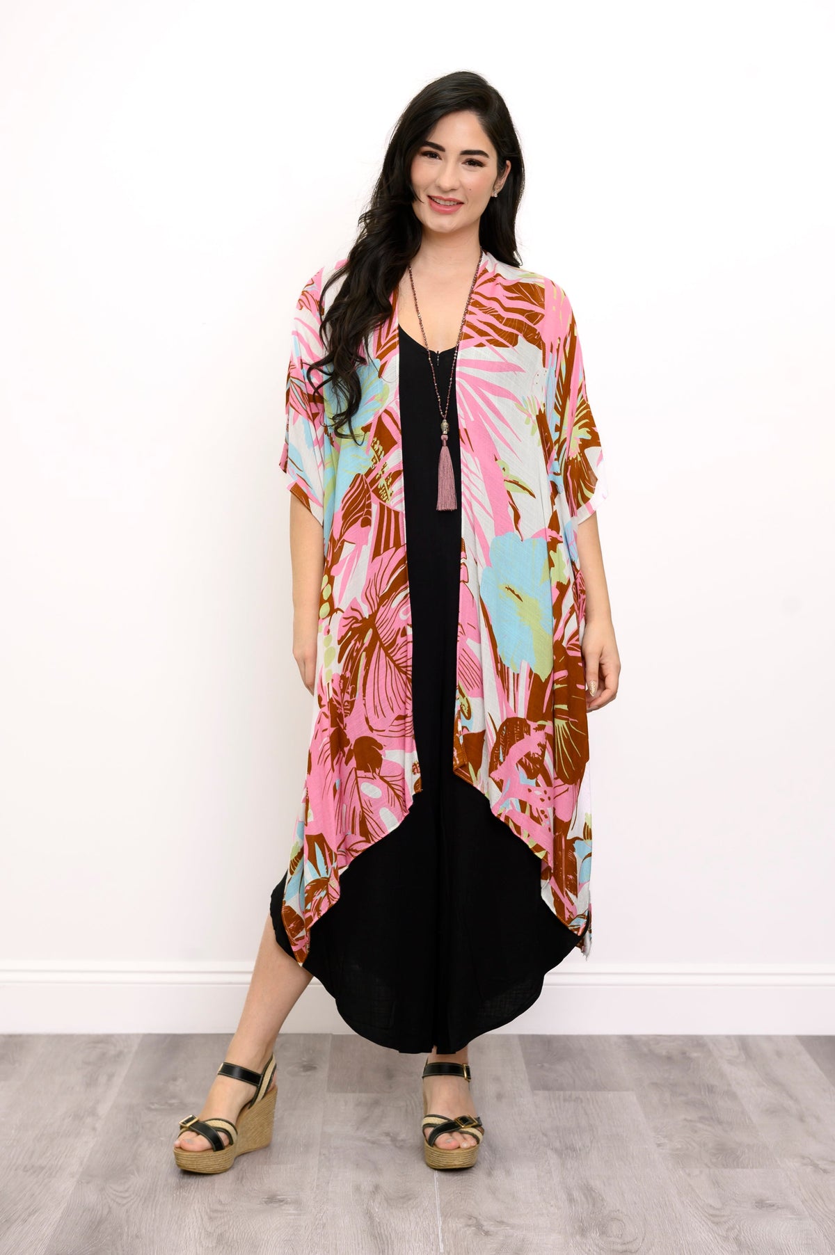 Front view of woman wearing multicolor tropcial patterned kimono on a black outfit against a white background