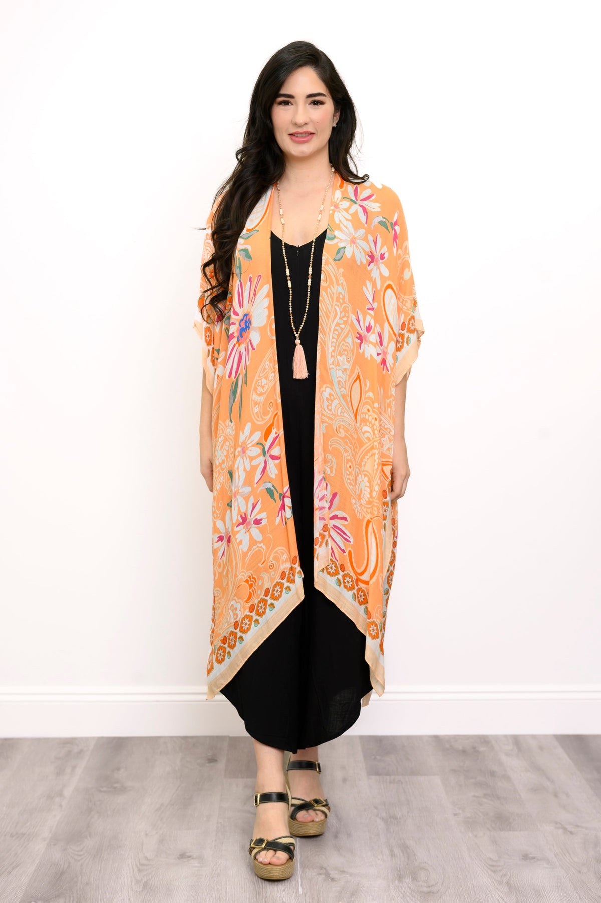 Front view of woman wearing orange floral patterned kimono on black outfit against a white background 