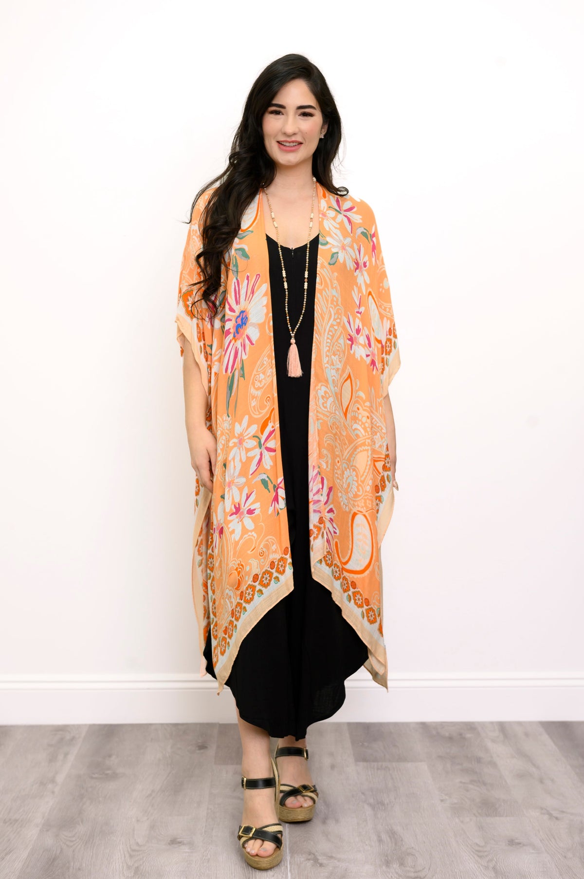 Front view of woman wearing orange floral patterned kimono on black outfit against a white background 