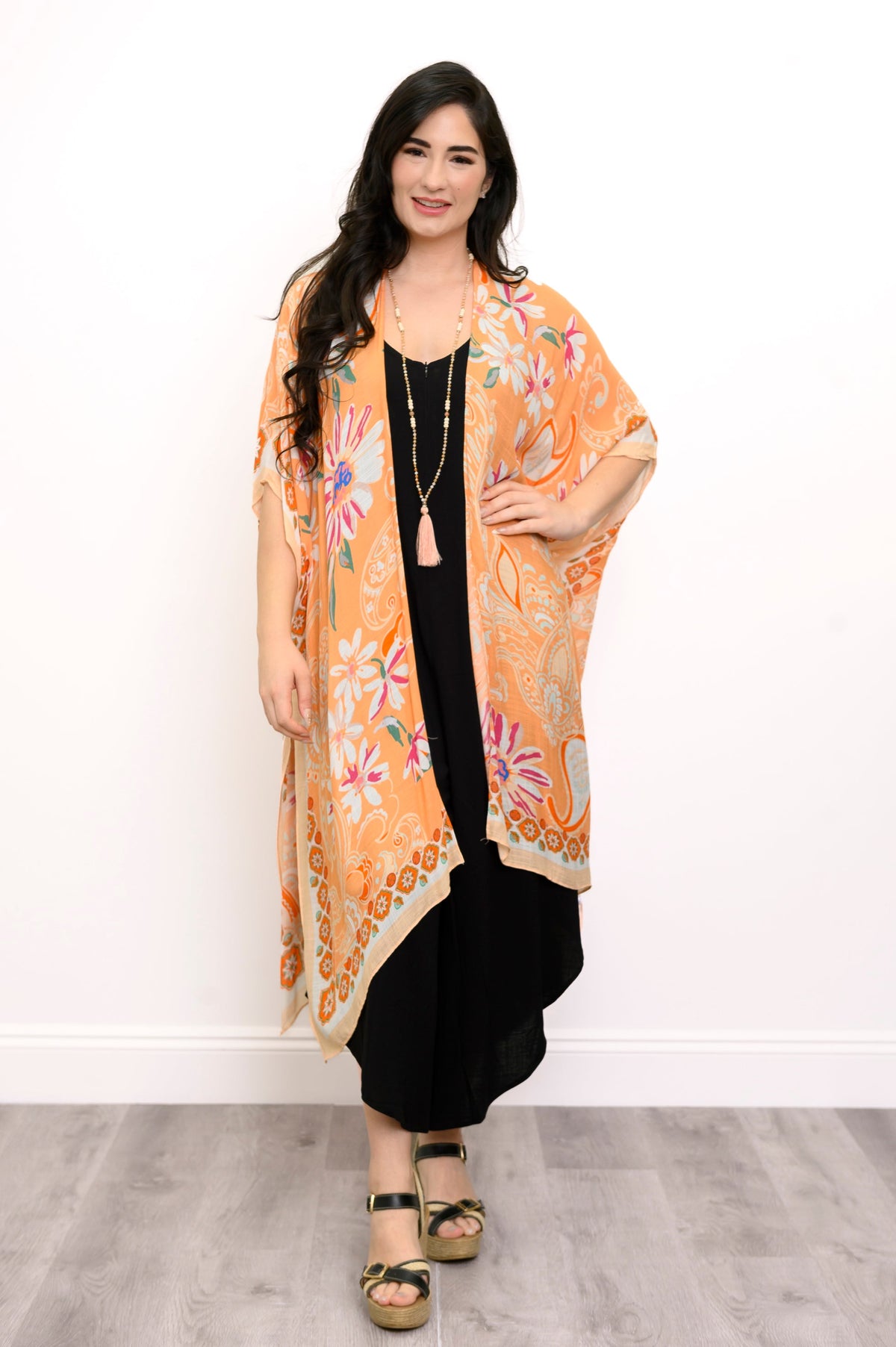 Front view of woman wearing orange floral patterned kimono on black outfit against a white background 