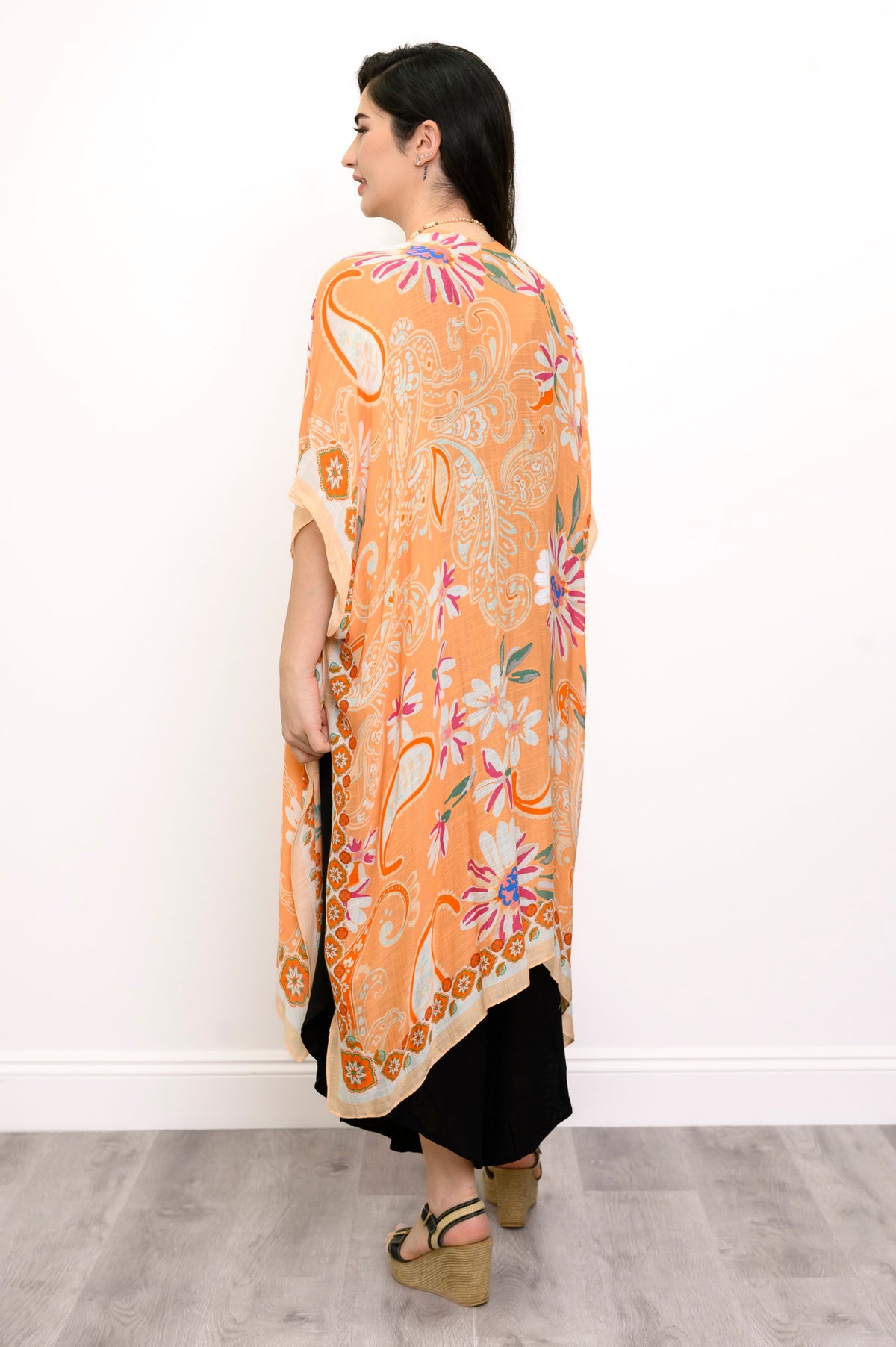 Back view of woman wearing orange floral patterned kimono on black outfit against a white background 