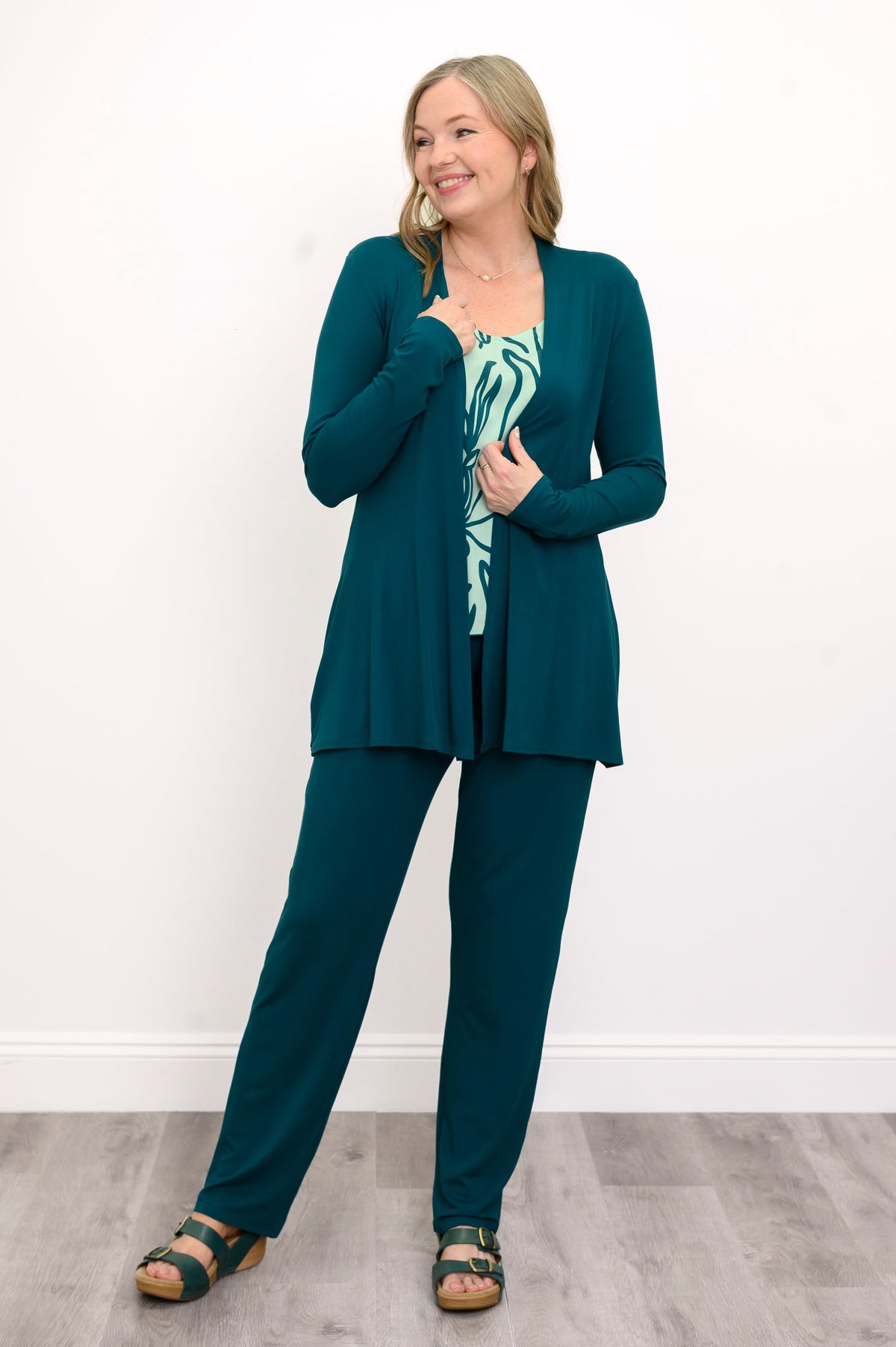 Front view, woman wearing a green sweater, green patterned top, and green pants on a white background
