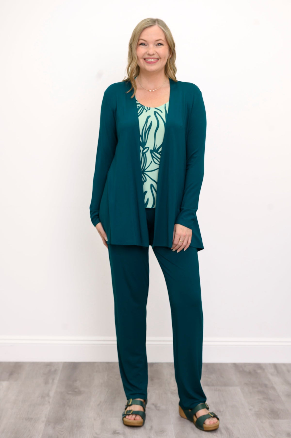 Front view, woman wearing a green sweater, green patterned top, and green pants on a white background