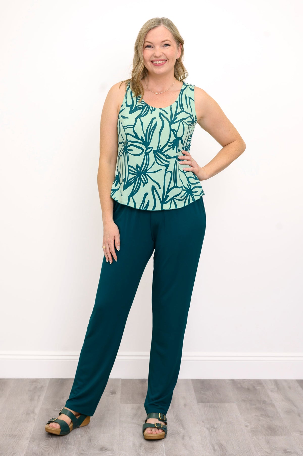 Front view of Woman wearing a green floral patterned sleeveless top and green pants against a white background