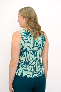 Back view of Woman wearing a green floral patterned sleeveless top and green pants against a white background