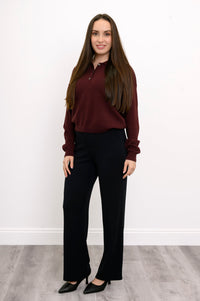 Angled view of woman wearing wine red long sleeve sweater and relaxed fit black pants