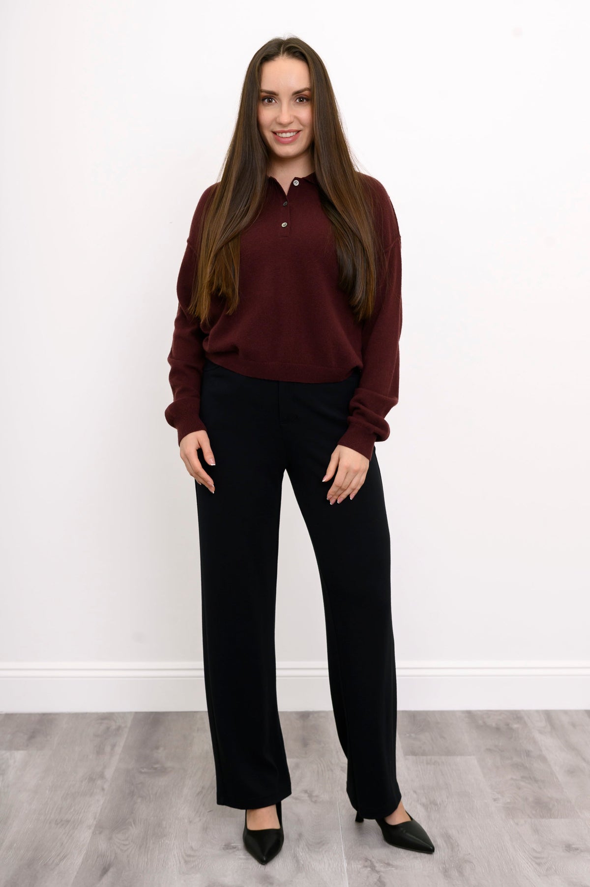 Full body front view of woman wearing loose fitting cashmere sweater with ribbed hem and dark cherry color
