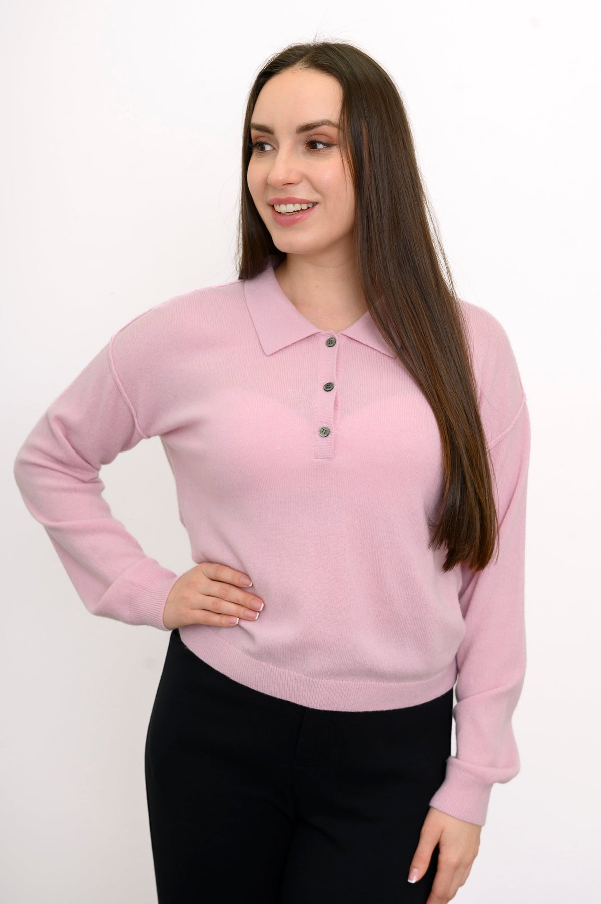 Woman wearing a pink collared knit sweater and denim pants on a white background, front view