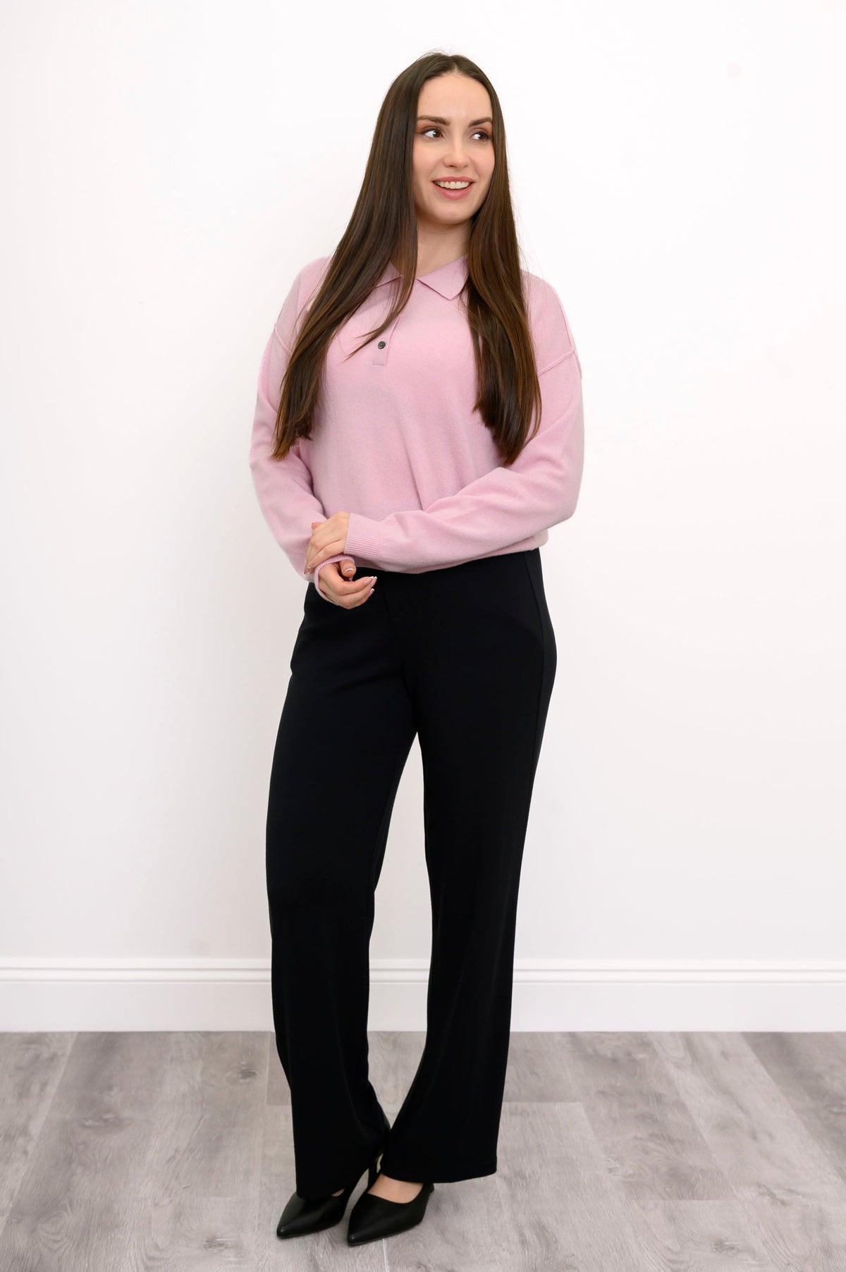 Full body view of model wearing relaxed fit cashmere sweater in light pink, styled with long black pants