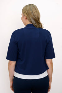 Back view, woman wearing navy blue jacket, white top and blue pants against a white background