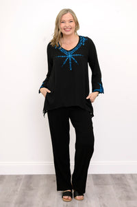 Front view of woman wearing a black top with blue embellishments and black pants against a white background