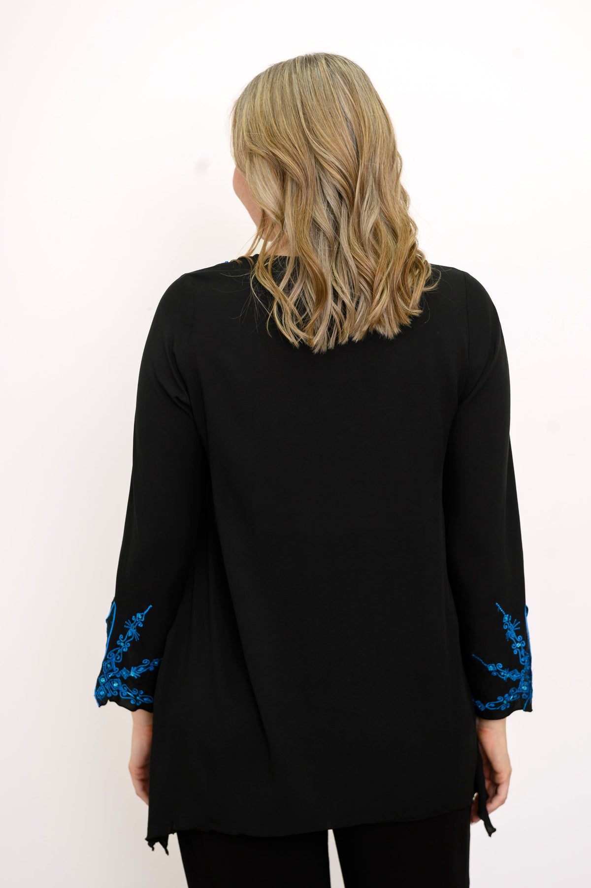 Back view of woman wearing a black top with blue embellishments and black pants against a white background