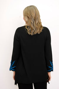 Back view of woman wearing a black top with blue embellishments and black pants against a white background