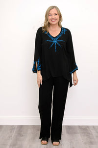 Front view of woman wearing a black top with blue embellishments and black pants against a white background