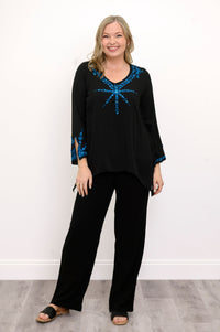 Front view of woman wearing a black top with blue embellishments and black pants against a white background