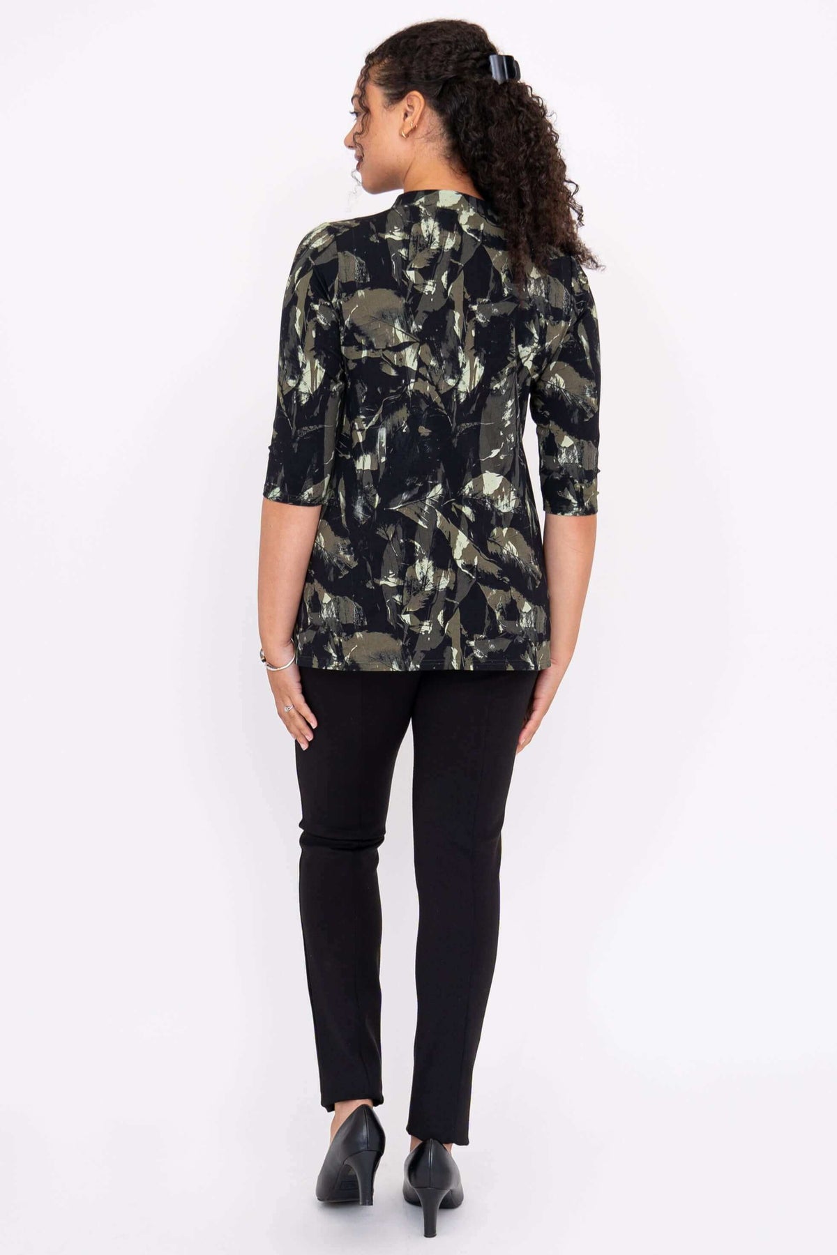 Back view of a woman wearing the black and green abstract patterned top, black pants, and heels