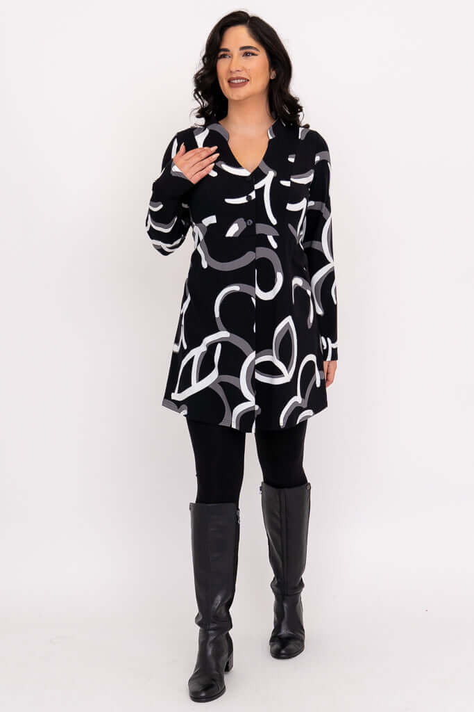 Woman smiling and gesturing in tunic, black with modern white and grey design.
