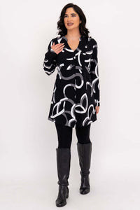 Woman smiling and gesturing in tunic, black with modern white and grey design.