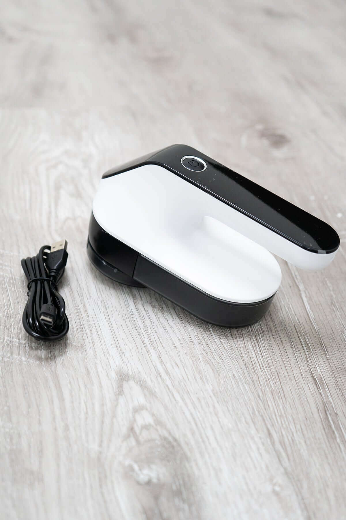 Electric lint remover in open position with USB charging cable on wooden background