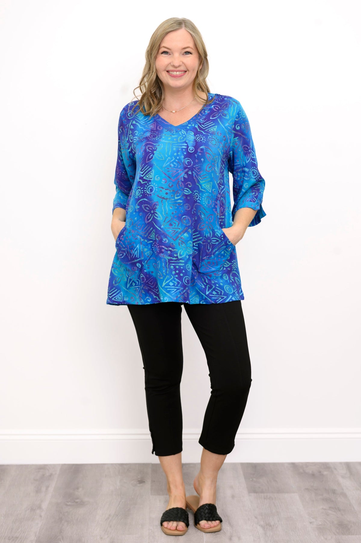 Front view of woman wearing a blue patterned blouse and black pants against a white background