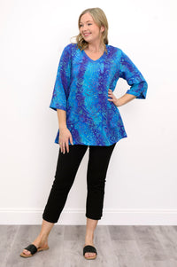 Front view of woman wearing a blue patterned blouse, black pants, and sandals against a white background