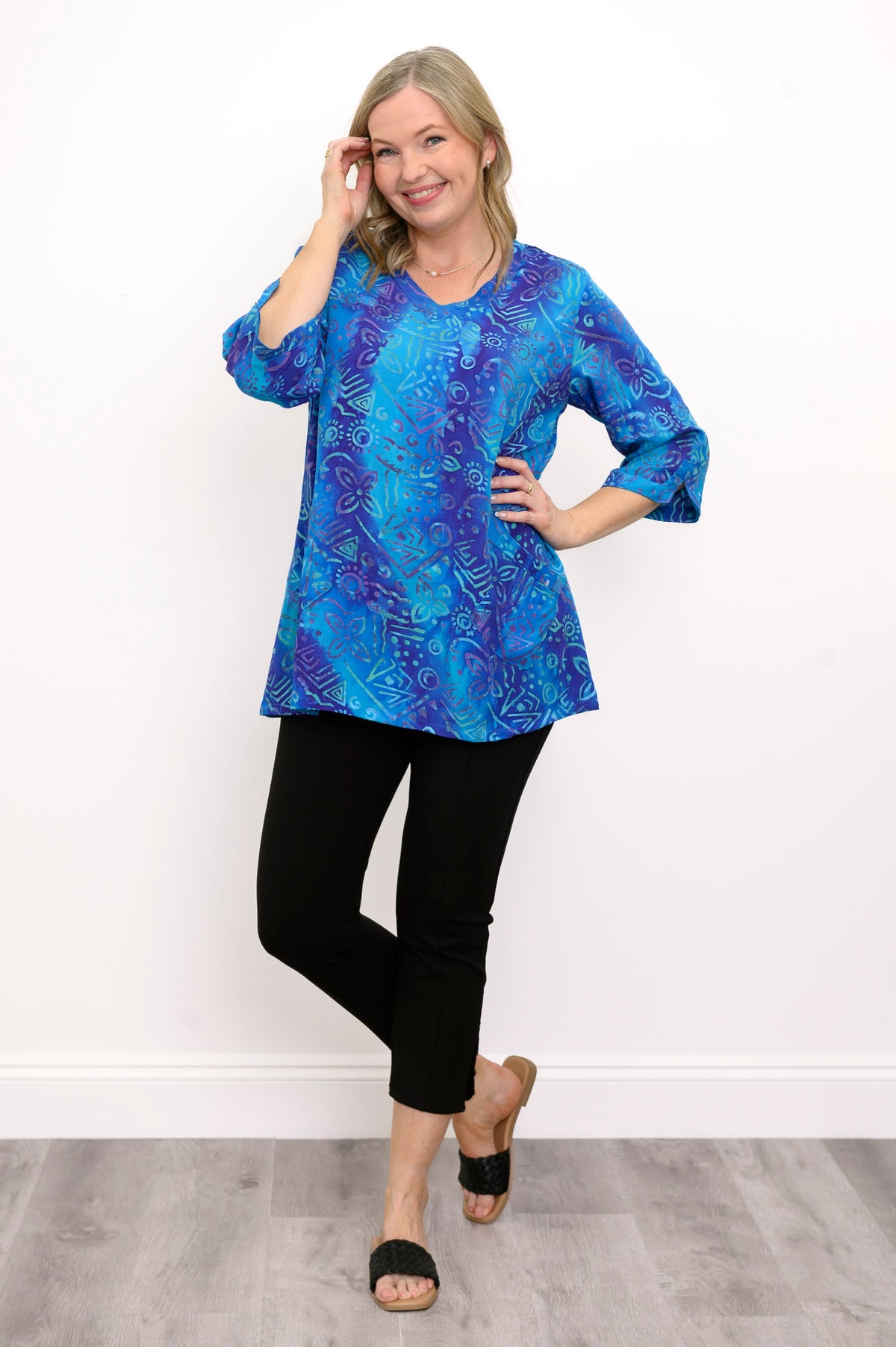 Front view of woman wearing a blue patterned blouse and black pants against a white background