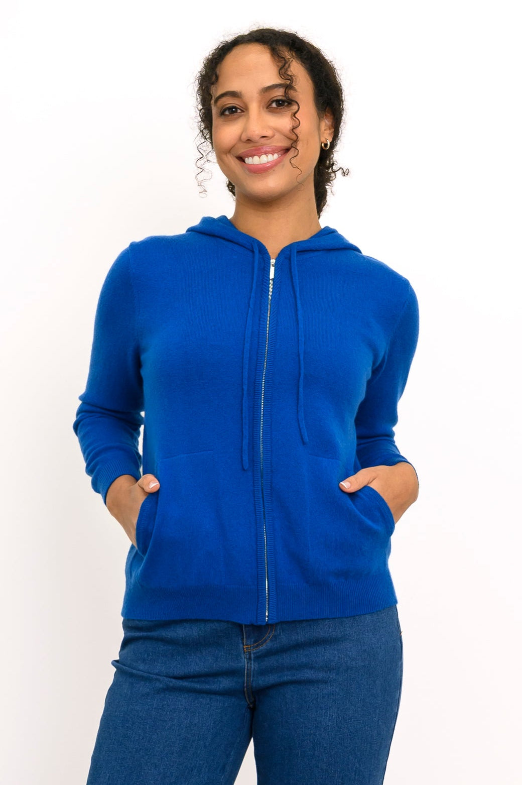 Close-up front view of woman smiling with her hands in the pockets of her cobalt blue knit hoodie