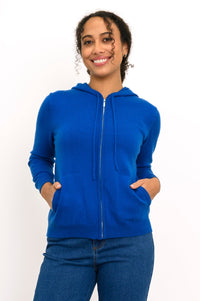 Close-up front view of woman smiling with her hands in the pockets of her cobalt blue knit hoodie