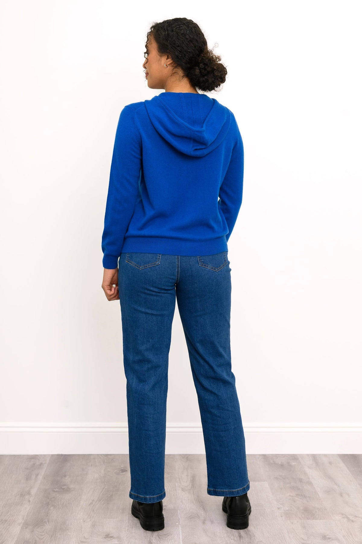 Full body back view of woman wearing bright blue hoodie with jeans and black boots