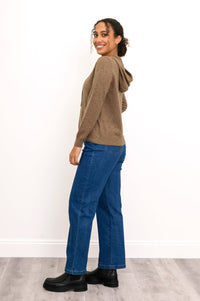 Woman wearing a knit brown hoodie with pockets and denim pants in front of a white background, side view