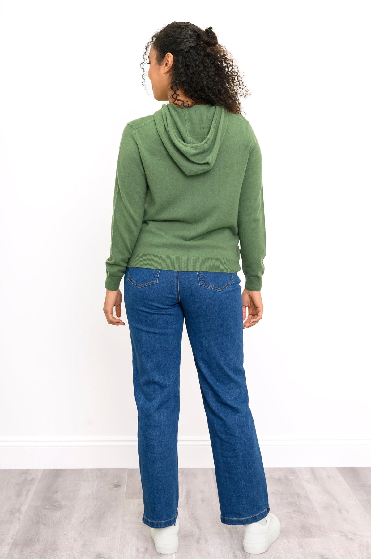 Full body back view of woman wearing cool-toned green hoodie with jeans and white sneakers