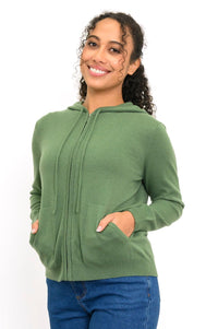 Woman wearing a knit green hoodie with pockets and denim pants in front of a white background, front view