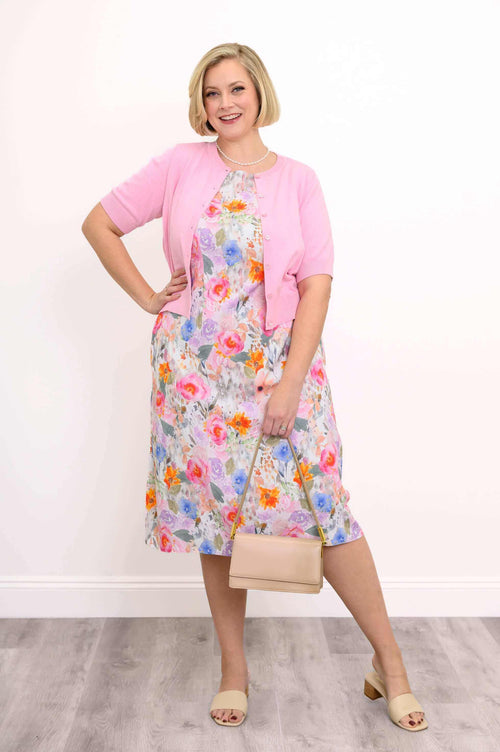 Woman in a floral shift dress styled with a pink cardigan and beige handbag