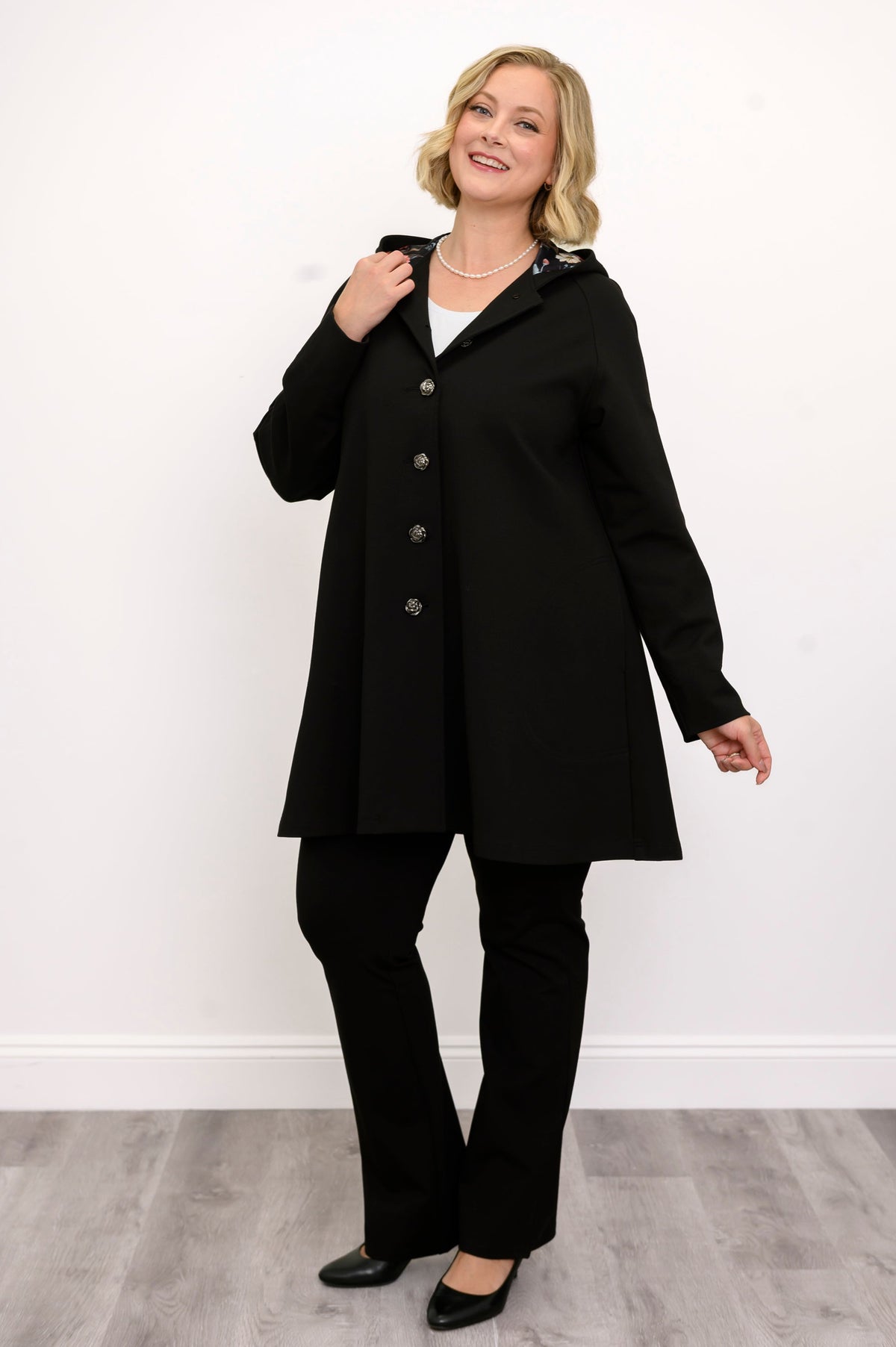 Full length front view of a woman wearing a black modal A-line coat paired with black trousers.