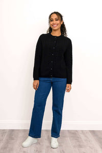 Woman standing front-facing in a black cardigan with blue jeans and white shoes