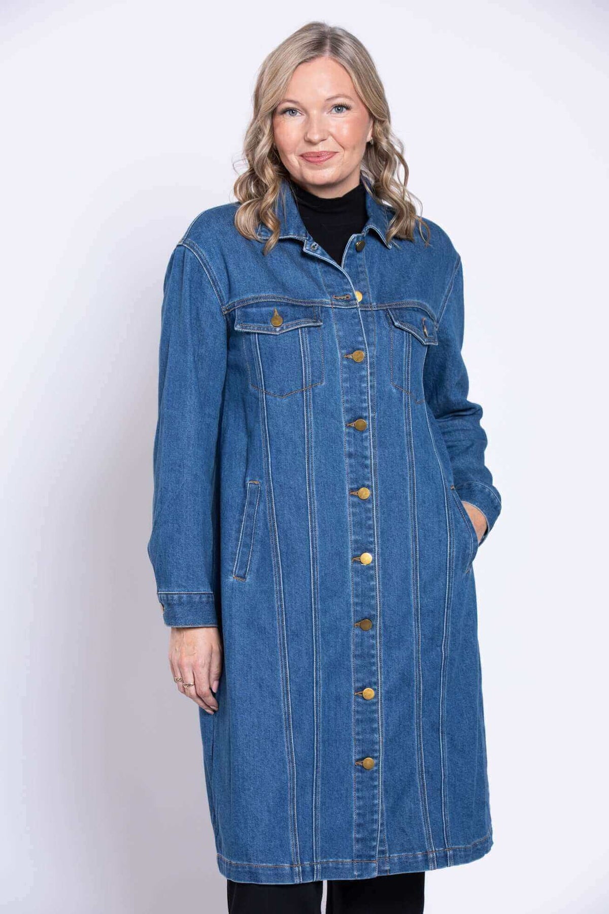 Woman smiling and putting her hand the pocket of the long denim coat she is wearing