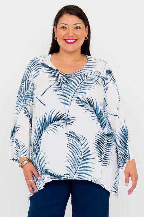 Woman wearing a white flowy top with blue palm print and navy pants, front view
