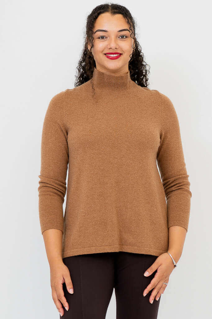 Front view of a woman wearing a camel brown mock neck sweater and dark pants