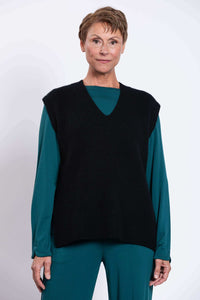 Front view of model wearing a black boxy V-neck sweater vest over teal top and pants