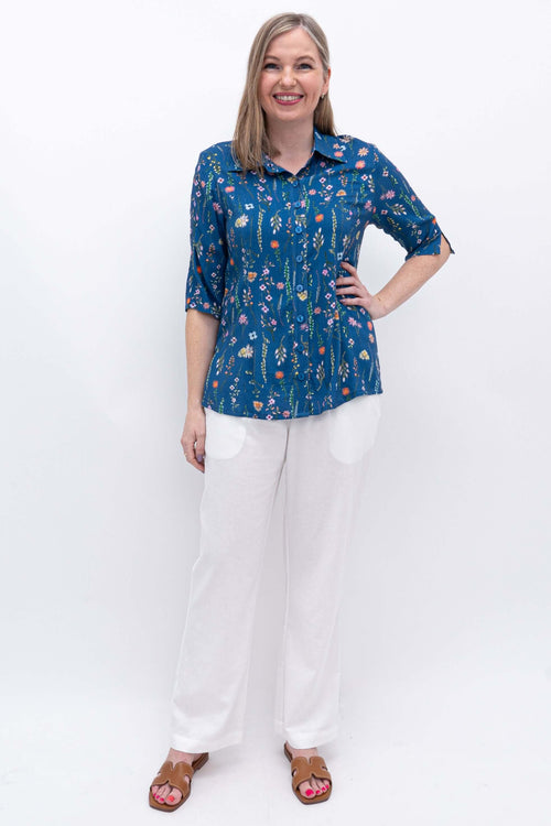 Model wearing a blue floral print blouse and white pants, full body front view