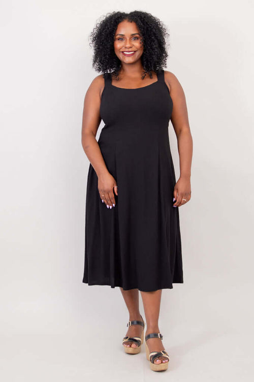Front view of model wearing a black A-line midi dress with wide straps